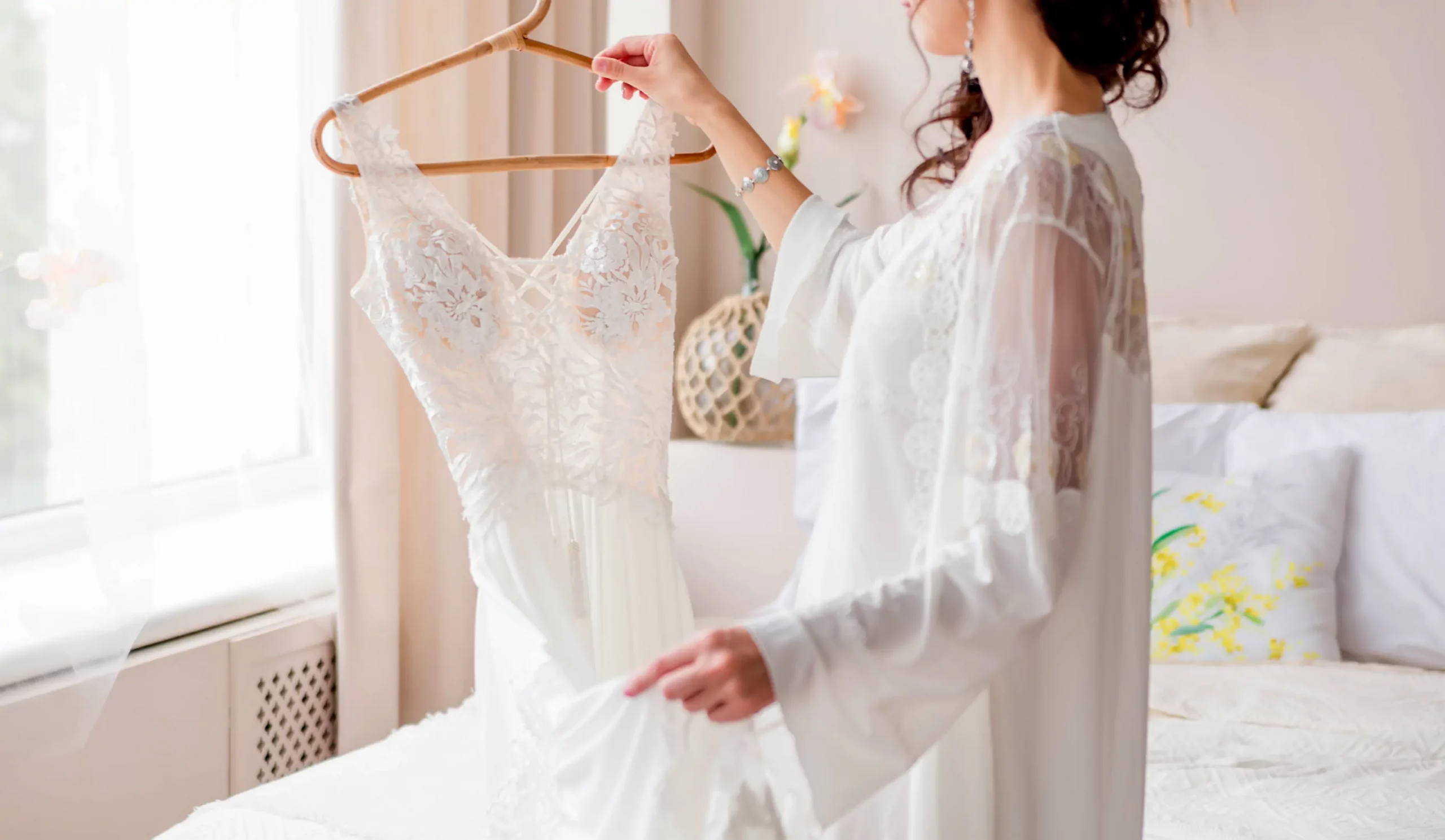 bride-white-peignoir-stands-near-bed-holds-wedding-dress-her-hands-horizontal-photo